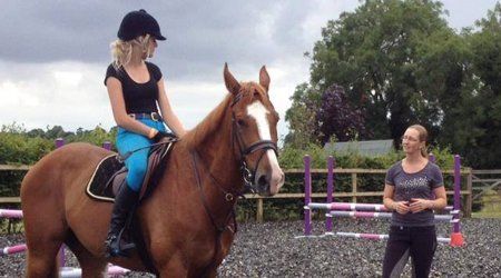Riding instructor teaching student on brown horse in outdoor arena